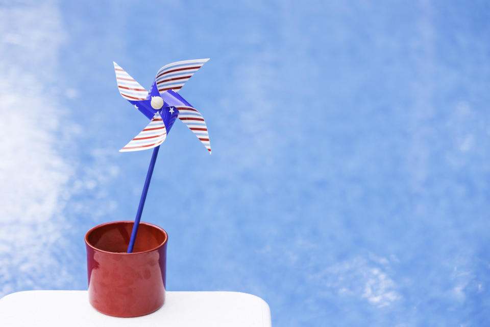 Red, white & blue pinwheel or whirligig in red pot with shimmering pool backdrop.