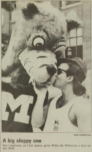 A newspaper clipping of an old photo showing a man giving a mascot version of Willy the Wolverine a kiss on the cheek.