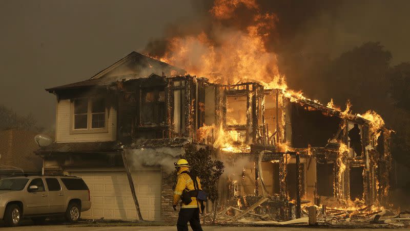 A firefighter walks near a flaming house in Santa Rosa, Calif., in this 2017 file photo. The largest property and casualty insurance company in the U.S. has said no to new customers in California hoping to build or buy a home, citing extreme wildfire risks in that state and dramatic increases in construction costs.