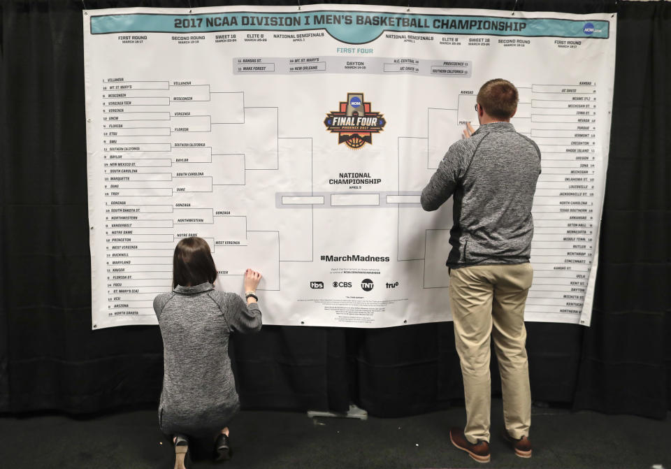 FILE - Staff members for the NCAA place the names of the teams in the Sweet 16 on a bracket in the media workroom before practices at the East Regional of the NCAA college basketball tournament in New York, March 23, 2017. College hoops fans might want to think again before pinning their hopes of a perfect March Madness bracket on artificial intelligence. While the advancement of artificial intelligence into everyday life has made “AI” one of the buzziest phrases of the past year, its application in bracketology circles is not so new. (AP Photo/Julie Jacobson, File)