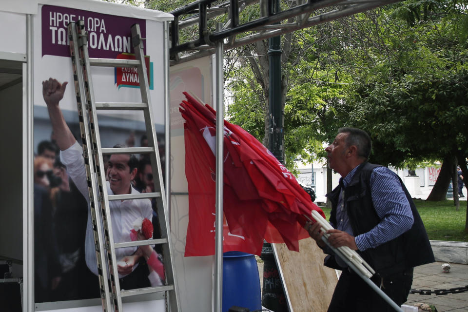 A photograph of Greece's Prime Minister Alexis Tsipras is displayed at a election kiosk of Syriza governing party as a worker carries flags at Syntagma square in Athens, Monday, May 27, 2019. Tsipras called snap general elections following a resounding defeat of his left-wing Syriza party in European elections. The poster reads "The time of the many has come." (AP Photo/Thanassis Stavrakis)