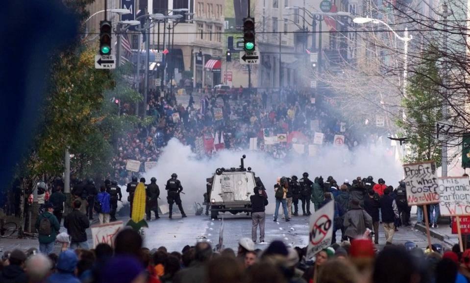 FILE - In this Nov. 30 1999, file photo, Seattle police use tear gas to push back World Trade Organization protesters in downtown Seattle. Saturday, Nov. 30, 2019 marks 20 years since tens of thousands of protesters converged on Seattle and disrupted a major meeting of the World Trade Organization. The protesters’ message was amplified not just by their vast numbers but by the response of overwhelmed police, who fired tear gas and plastic bullets and arrested nearly 600 people. Two decades later, many of their causes are still relevant. (AP Photo/Eric Draper, File)