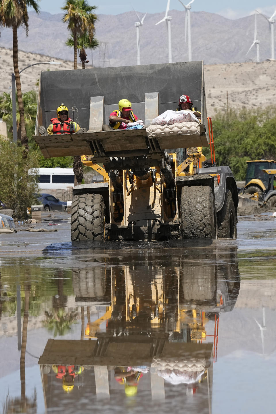 Firefighters use a skip loader to rescue people from an assisted living center after the street was flooded with mud, Monday, Aug. 21, 2023, in Cathedral City, Calif. (AP Photo/Mark J. Terrill)
