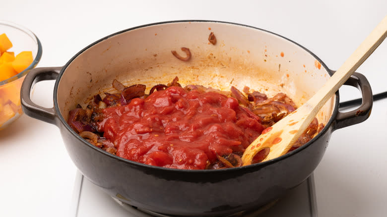 adding chopped tomatoes to pan