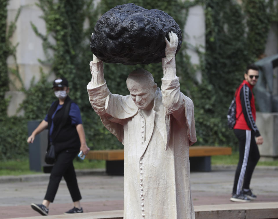 Visitors to the National Museum walk past a new statue of the late pope, St. John Paul II, throwing a stone at a "Poisoned Well" just hours before its official inauguration in the museum yard in Warsaw, Poland, Thursday, Sept. 24, 2020. The sculpture by Poland's Jerzy Kalina is said to be a response to a controversial 1999 sculpture by Italian Maurizio Cattelan in which the Polish-born pontiff was shown as being crushed by a similar stone. (AP Photo/Czarek Sokolowski)