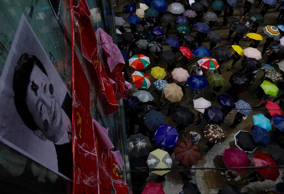 Protesters carrying umbrellas march past a pedestrian bridge displaying vandalized photos of Chinese President Xi Jinping and communist party flags in Hong Kong, Sunday, Oct. 6, 2019. A group of pro-democracy Hong Kong legislators filed a legal challenge against the government's use of a colonial-era emergency law to criminalize the wearing of masks at rallies to quell anti-government demonstrations, which diminished in intensity but didn't stop. (AP Photo/Vincent Yu)