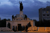 A couple with their dog walk in front of the Liberty monument in central capital Nicosia, Cyprus, Wednesday, Jan. 27, 2021. Cyprus' health minister Constantinos Ioannou said that the first to re-open as of Feb. 1st will be hair and beauty salons followed a week later by retail stores, shopping malls and elementary schools. Students in their final year of high school will also go back to classes on Feb. 8. (AP Photo/Petros Karadjias)