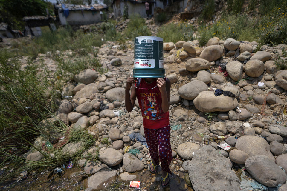 FILE- A girl covers her head with a repurposed container to shield herself from the sun as she walks to collect water from a leaking municipal pipe on a hot summer day on the outskirts of Jammu, India, Friday, May 31, 2024. Officials say a scorching heat wave has killed at least 14 people, including 10 election officials, in eastern India with temperatures soaring up to 49.9 degrees Celsius (122 degrees Fahrenheit) in parts of India this week. (AP Photo/Channi Anand, File)