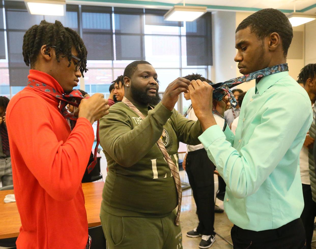 Markell Yates, 17, works on tying his tie as coach Antonio Goodwin helps Jonathan White with his tie during a recent resume writing and interview workshop at Firestone high school.