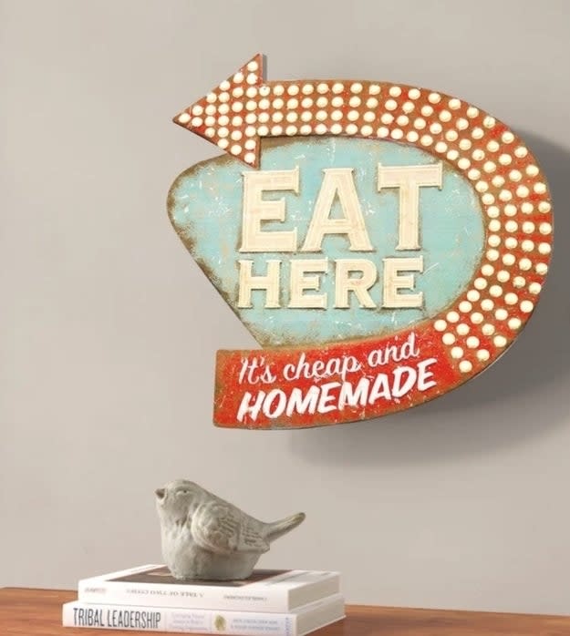 Vintage "EAT HERE" sign with arrow, perched atop books beside a bird figurine