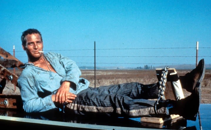 A prisoner sits on a car while smoking a cigarette.