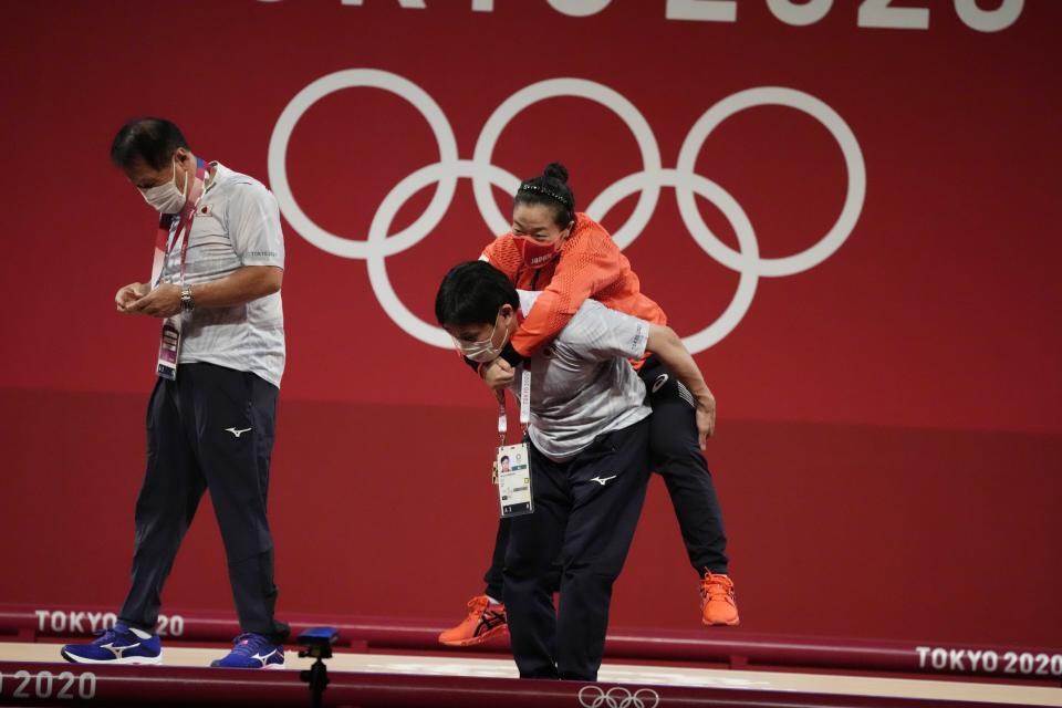 Mikiko Andoh of Japan cis carried by her coach Naoyuki Kobatake after winning the bronze medal in the women's 59kg weightlifting event, at the 2020 Summer Olympics, Tuesday, July 27, 2021, in Tokyo, Japan. She won gold medal and sets a new Olympic record. (AP Photo/Luca Bruno)