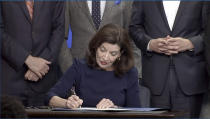 In this image taken from video, New York Gov. Kathy Hochul signs an executive order during a news conference, Wednesday, May 18, 2022, in New York. New York would require state police to seek court orders to keep guns away from people who might pose a threat to themselves or others under a package of executive orders and gun control bills touted Wednesday by Hochul in the aftermath of a racist attack on a Buffalo supermarket. (Office of the Governor of New York via AP)