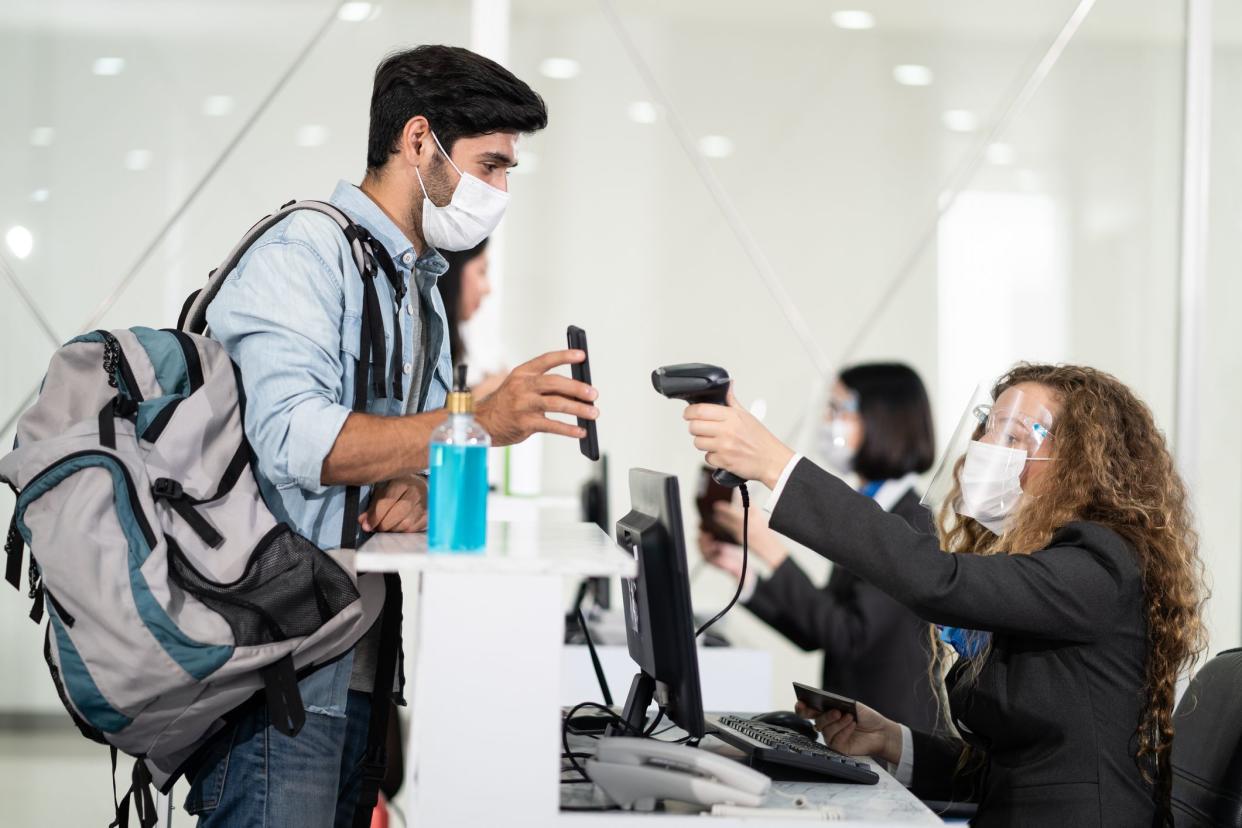 Male traveler shows phone to female officer at airline check in counter for issue airplane ticket boarding pass. Woman staff wear face mask to prevent from coronavirus pandemic. New normal lifestyle