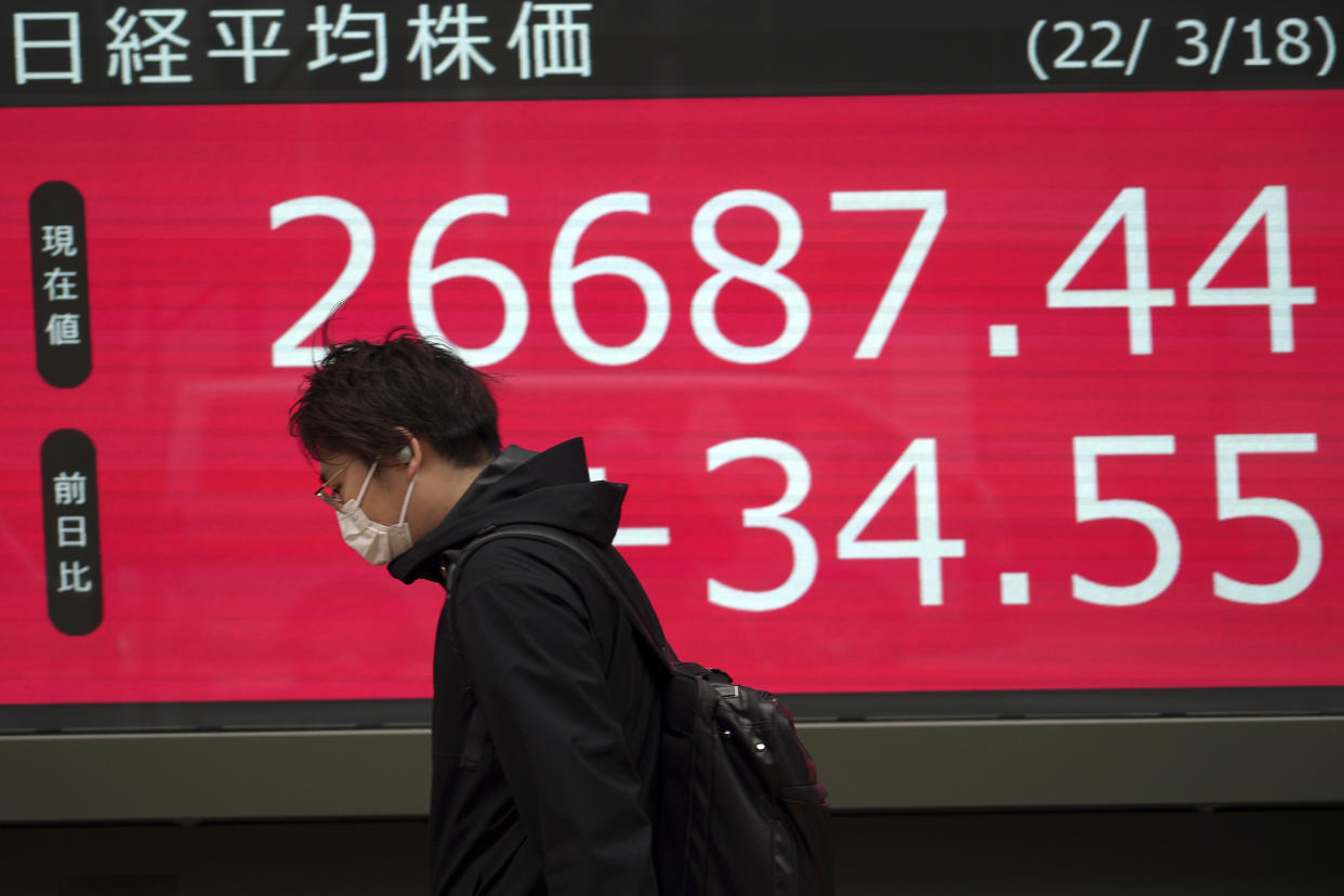 A man wearing a protective mask walks in front of an electronic stock board showing Japan's Nikkei 225 index at a securities firm Friday, March 18, 2022, in Tokyo. Shares were mostly lower in Asia on Friday after Wall Street extended a rally into a third day and oil prices pushed higher, surpassing $105 per barrel. (AP Photo/Eugene Hoshiko)