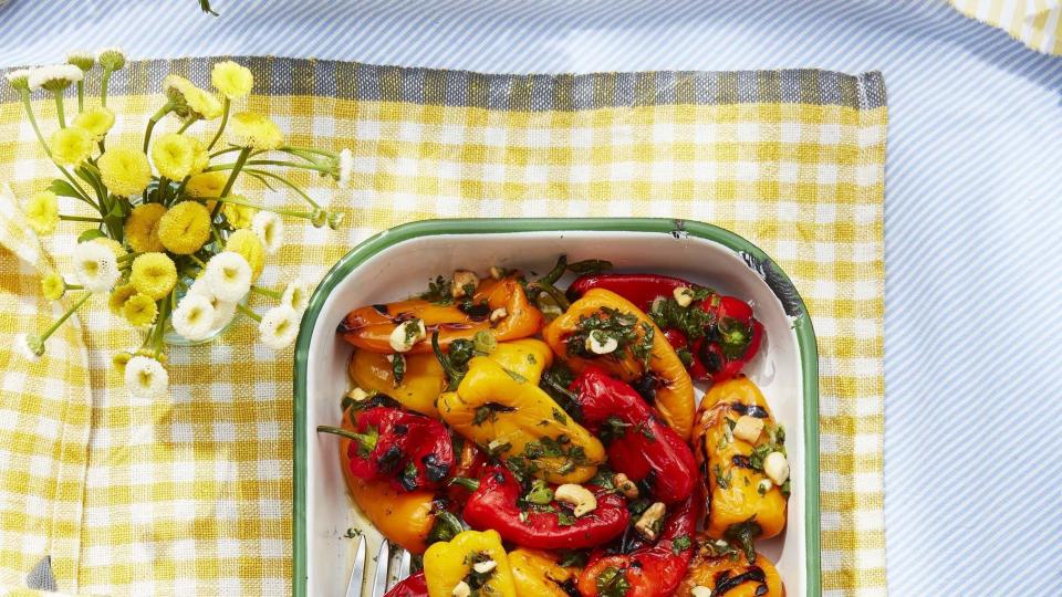 charred baby peppers with lime and cashew vinaigrette in a white serving tray with green trim on a yellow gingham tablecloth
