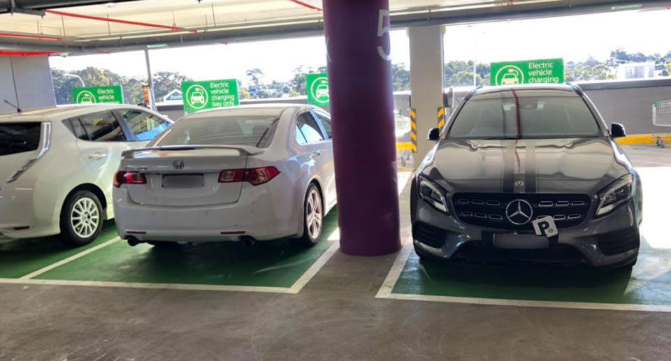 Two conventional cars parked in EV charging spots at a shopping centre.