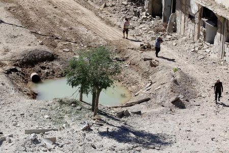 People walk past a hole in the ground filled with water in a damaged site after airstrikes on the rebel held Tariq al-Bab neighbourhood of Aleppo, Syria September 24, 2016. REUTERS/Abdalrhman Ismail