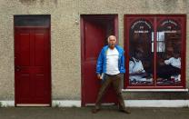 A man stands in front of an empty building, which has been covered with artwork to make it look more appealing, in the village of Bushmills on the Causeway Coast August 19, 2013. One of the homes of Irish whiskey has taken a scheme developed in Northern Ireland of erecting fake shop fronts where derelict buildings lie and has truly run with it in a bid to woo tourists. Bushmills, best known as the village where the whiskey of the same name was distilled for the first time 400 years ago, is now also becoming recognisable for the artwork and graphics that brighten up shop fronts left empty during the economic downturn. Picture taken August 19, 2013. REUTERS/Cathal McNaughton (NORTHERN IRELAND - Tags: BUSINESS SOCIETY TRAVEL) ATTENTION EDITORS: PICTURE 16 OF 20 FOR PACKAGE 'NORTHERN IRELAND'S TROMPE L'OEIL' SEARCH 'BUSHMILLS ART' FOR ALL IMAGES