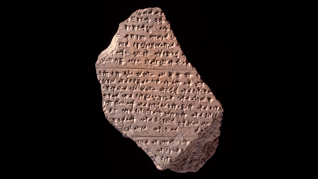  A broken clay tablet with cuneiform against a black background.  . 