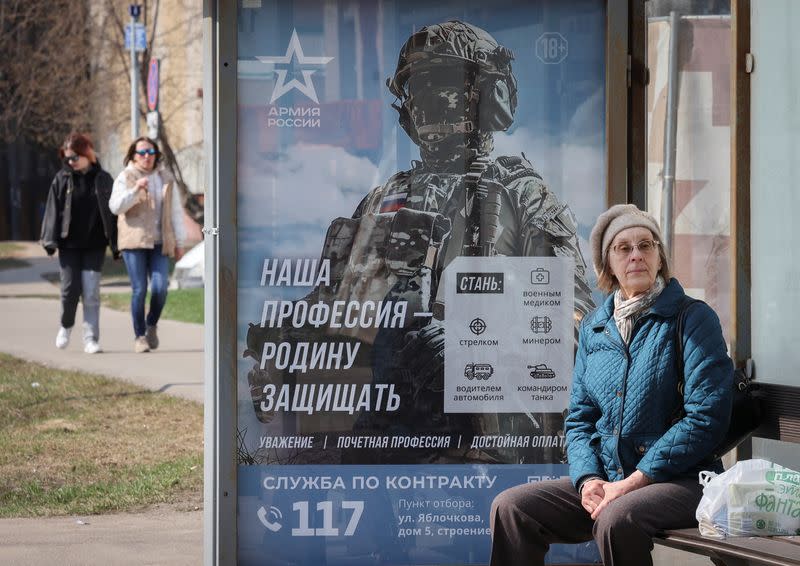 FILE PHOTO: A woman waits at a bus stop next to a poster promoting Russian army service in Moscow