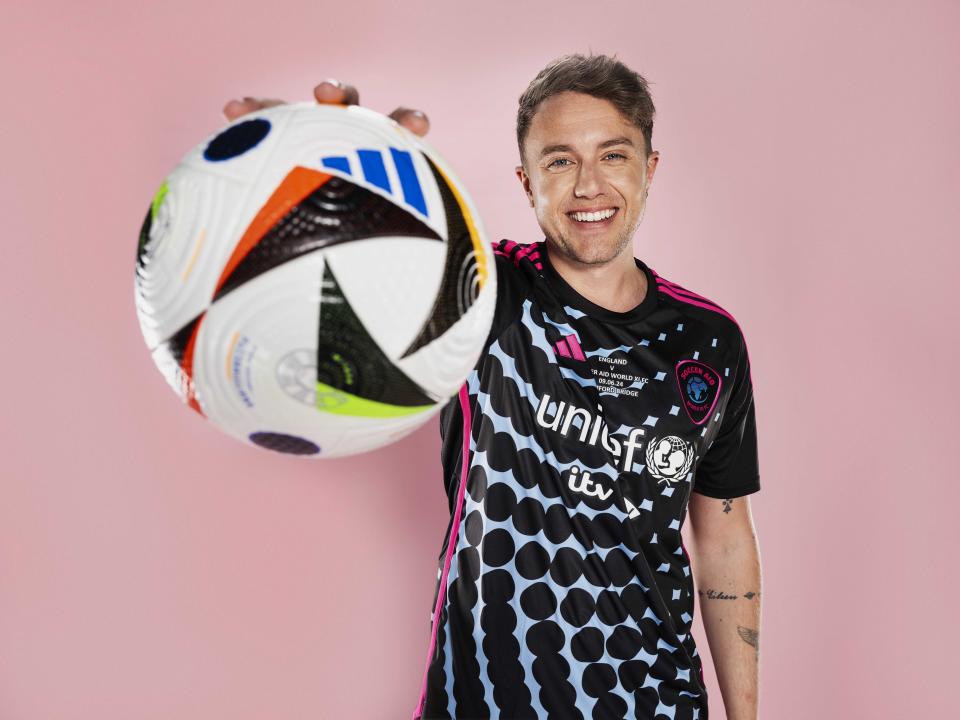 Roman Kemp wearing a black Soccer Aid football kit and holding a football