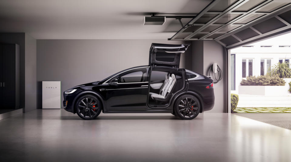 A black Tesla Model X in a garage with its falcon wing doors open.