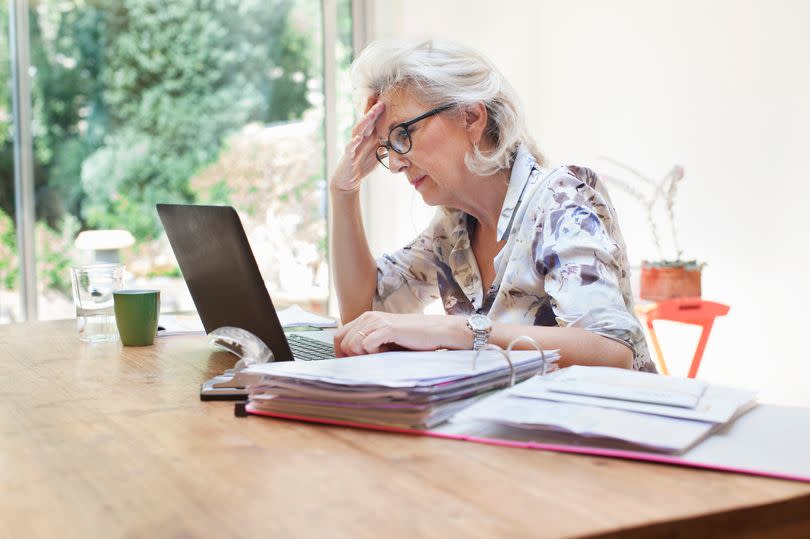 A woman sitting at a table with a laptop and folder looking worried over finances