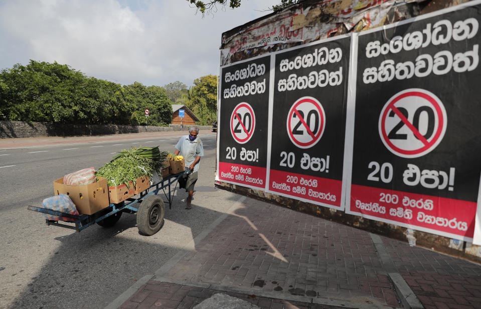 A Sri Lankan vegetable seller pushes his cart past posters against a proposed constitutional amendment that would consolidate power in the president’s hands in Colombo, Sri Lanka, Tuesday, Oct. 20, 2020. Sinhalese reads " No to 20 even with amendments". (AP Photo/Eranga Jayawardena)