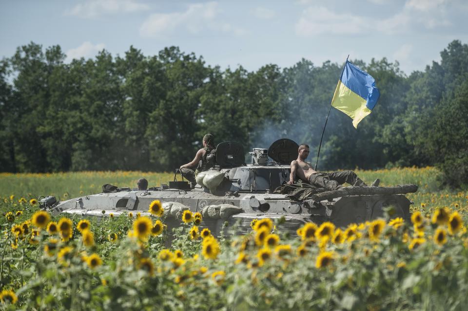 FILE - Ukrainian troops ride on an APC with a Ukrainian flag, in a field with sunflowers in Kryva Luka, eastern Ukraine, on July 5, 2014. (AP Photo/Evgeniy Maloletka, File)