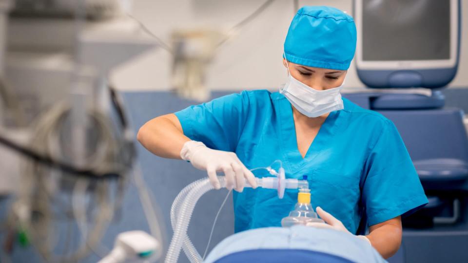 Nurse anesthetist putting oxygen mask to patient during surgery