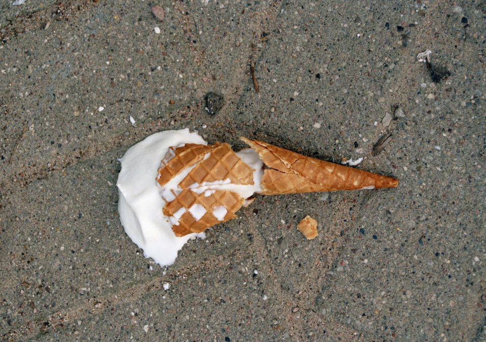 A dropped ice cream cone with a scoop of vanilla ice cream on the ground
