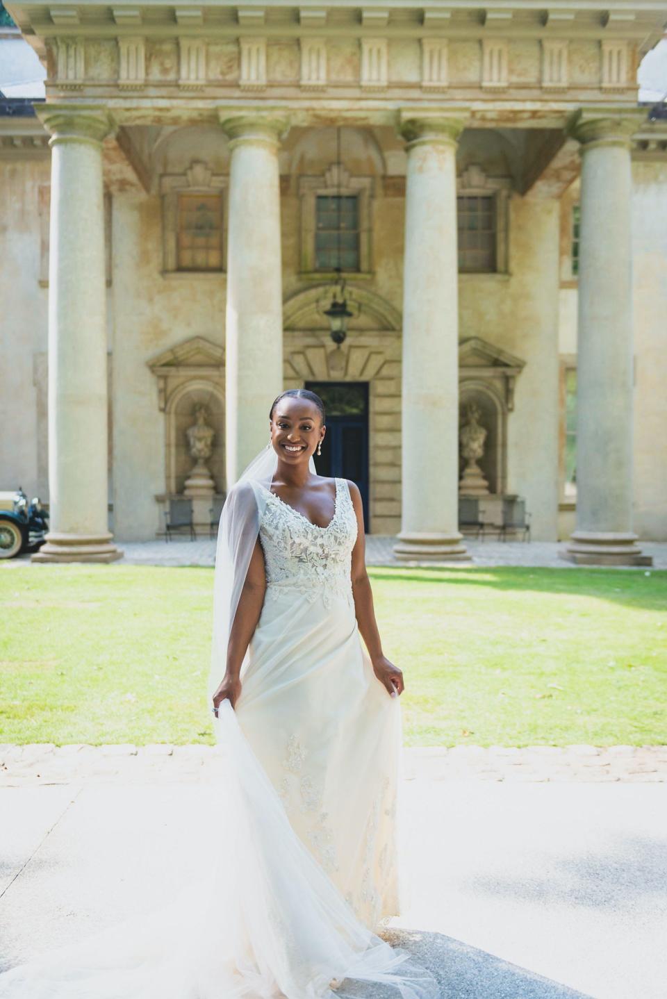 A bride poses in her wedding dress in front of a mansion.