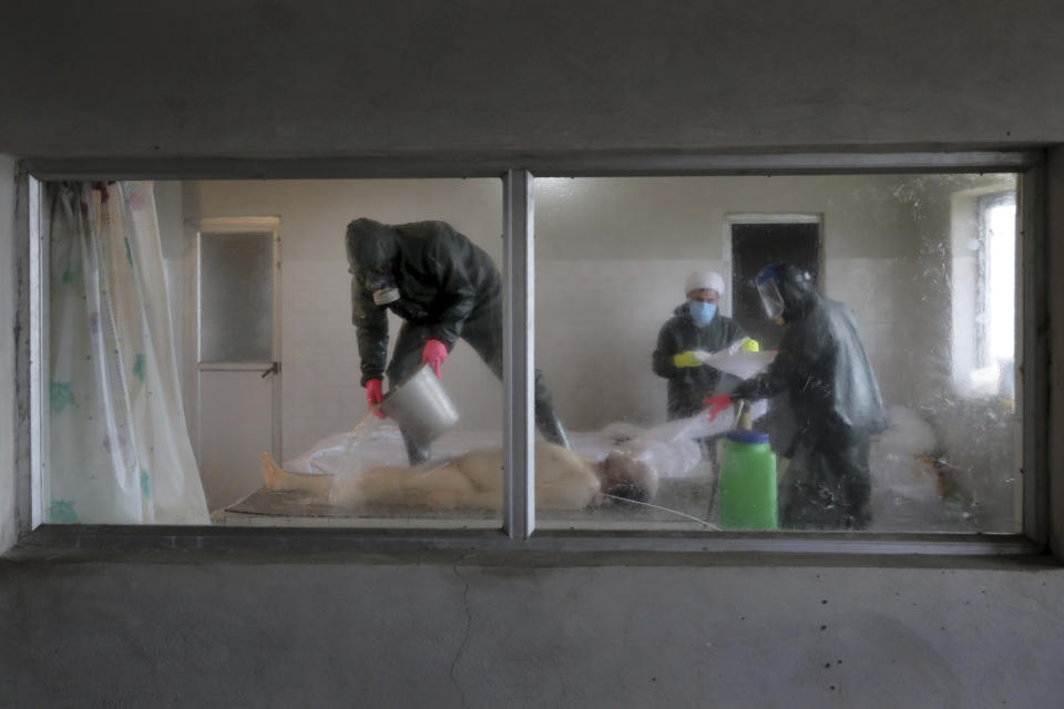 Hassan Khabir, 31, left, Ali Rahimi 53, center, and Mohammad Hossein Khoshnazar, 18, right, volunteer clerics wearing protective clothing, prepare the body of a 59-year-old man who died from COVID-19 for burial on the outskirts of the city of Ghaemshahr, in northern Iran, Dec. 19, 2020. Associated Press photographer Ebrahim Noroozi says of the image: “I was filled with so much grief and sorrow; seeing the body of that dead man in such a cold and dark room that I could not even raise my camera to take a picture” at first. “But the devotion and sacrifice of the three volunteers,” who have buried some 500 bodies, “are the rays of hope ... We should still stay hopeful.” (AP Photo/Ebrahim Noroozi)