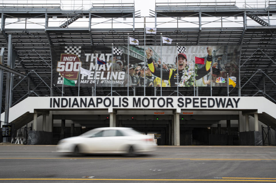 A car drives past the entrance at the Indianapolis Motor Speedway in Indianapolis, Saturday, March 28, 2020. Roger Penske, at 83 and considered high risk to the coronavirus as a 2017 kidney transplant recipient, still makes the daily three-minute commute to his Bloomfield Hills, Mich, office. He works 12 or more hours a day from his conference room at Penske Corp., which has a skeleton crew all practicing social distancing. Penske also had the small matter of planning his first Indianapolis 500. (AP Photo/Michael Conroy)