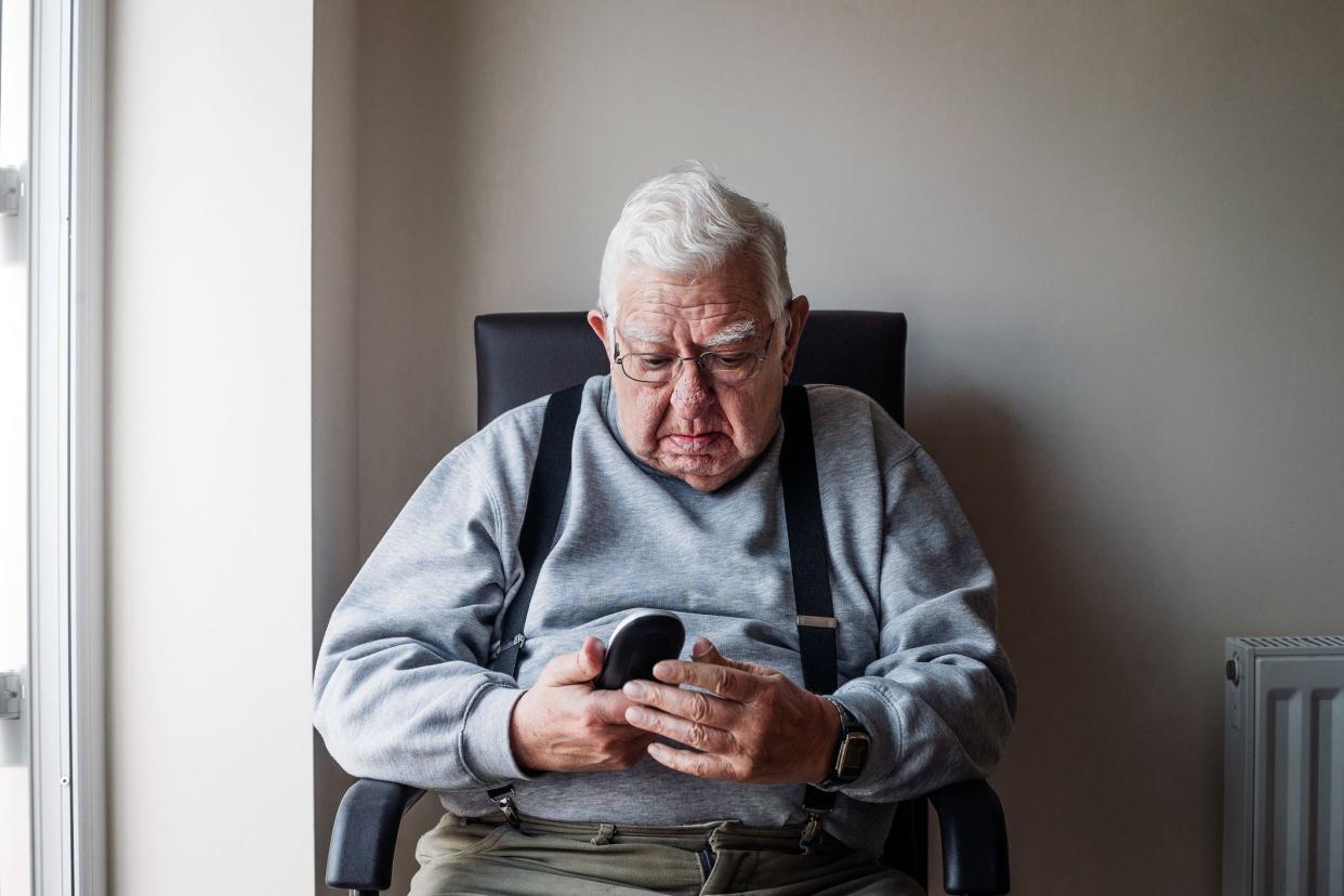 senior man seated looking at phone with concerned expression
