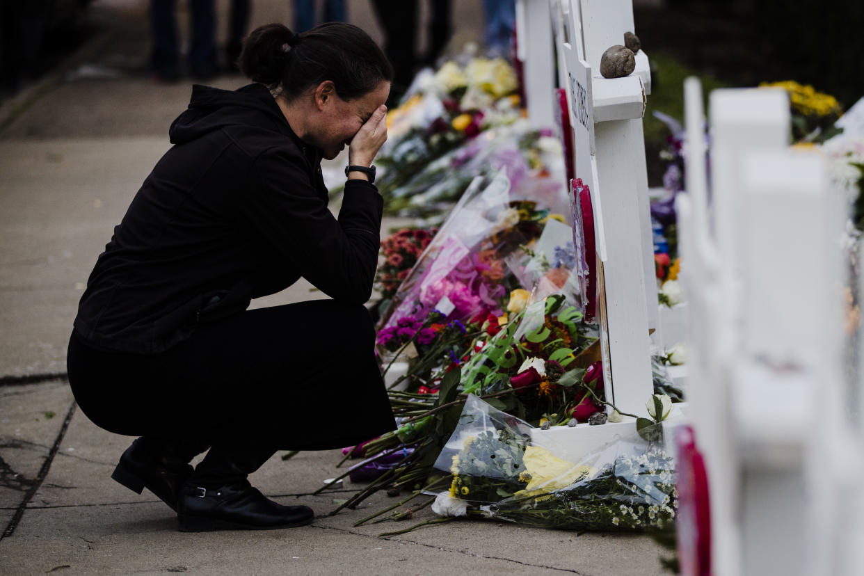 A woman dressed in black crouches, face in hands in front of a memorial on a sidewalk.
