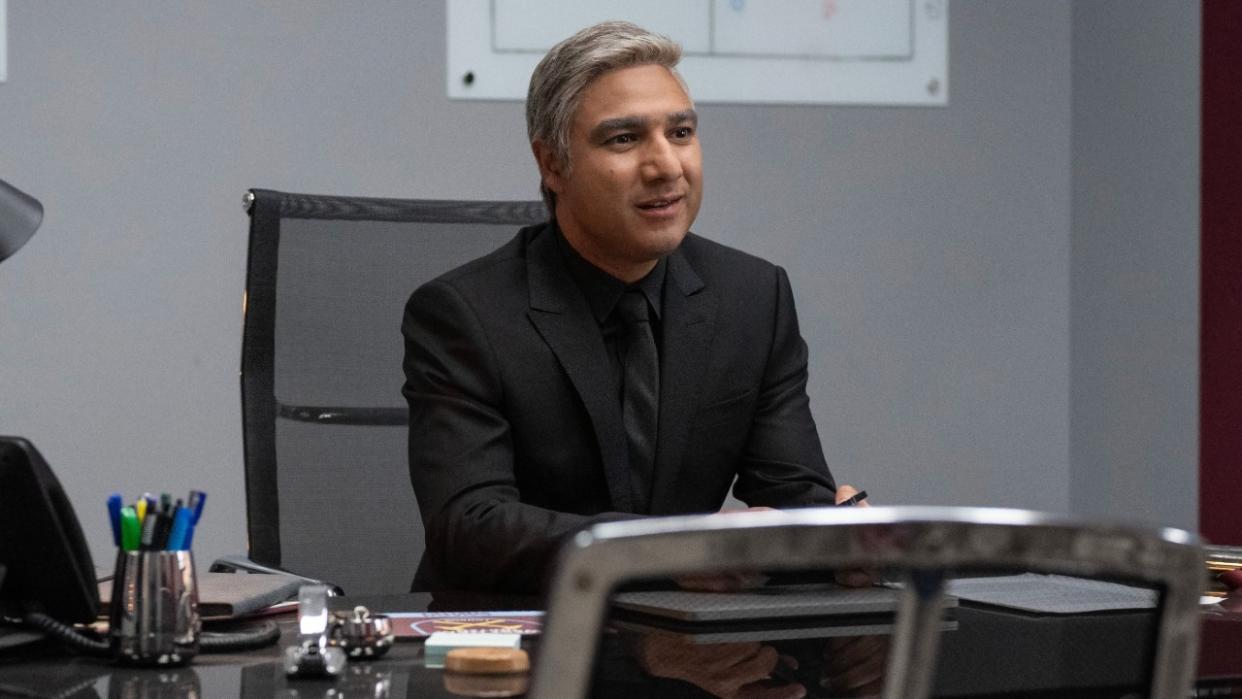  Nick Mohammed as Nate in a black suit sitting at his desk in Ted Lasso. 