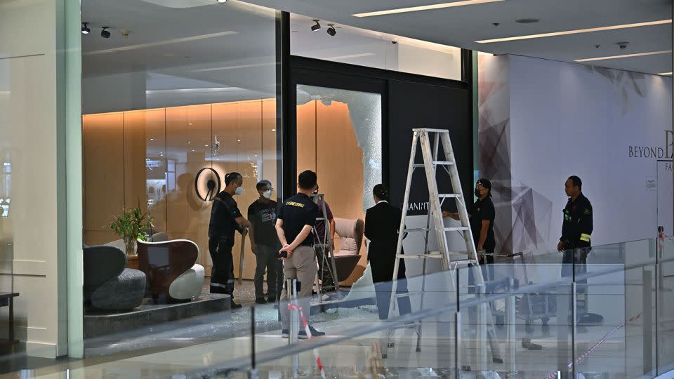 Staff repair the glass doors of a furniture store where a 14-year-old suspect was apprehended after a shooting rampage in Bangkok.
 - Lillian Suwanrumpha/AFP/Getty Images