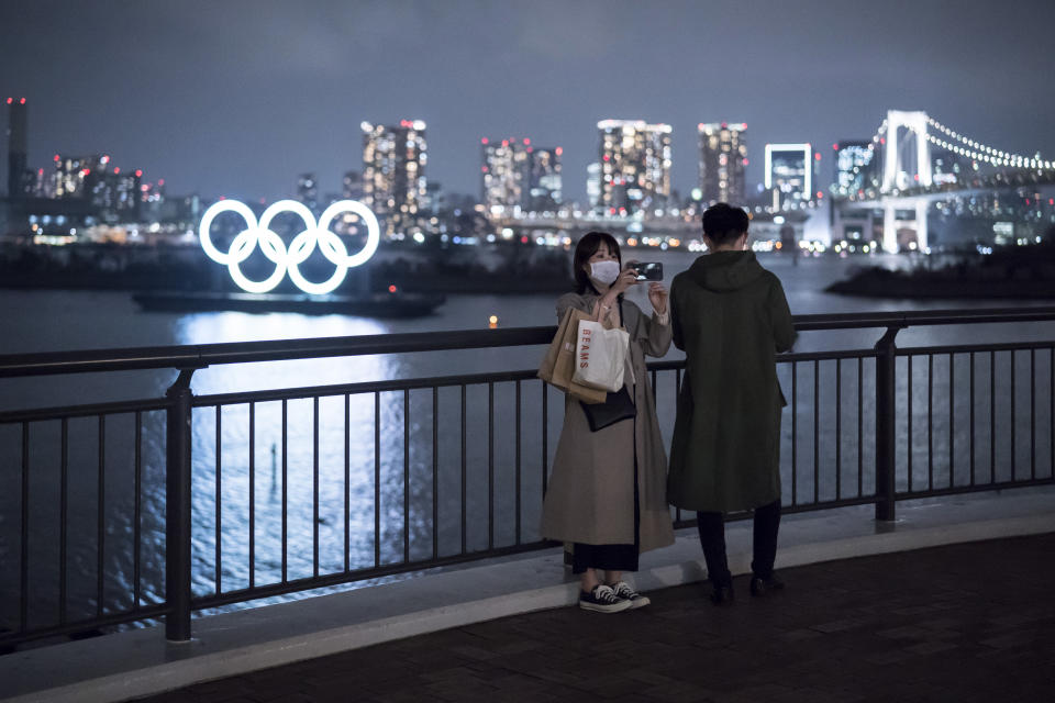 TOKYO, JAPAN - FEBRUARY 26: A woman wearing a face mask uses a smartphone as she takes a photograph in front of the Olympic rings at night on February 26, 2020 in Tokyo, Japan. Concerns that the Tokyo Olympics may be postponed or cancelled are increasing as Japan confirms 862 cases of Coronavirus (COVID-19) and as some professional sporting contests are being called off or rescheduled and some major Japanese corporations ask for people to work from home. (Photo by Tomohiro Ohsumi/Getty Images)