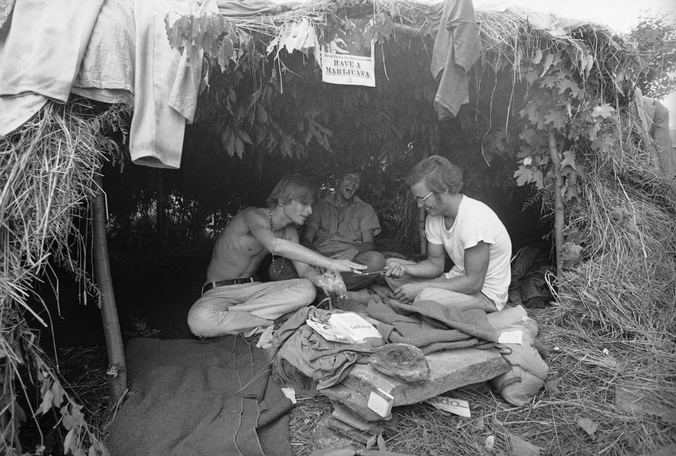 FILE - This Aug. 17, 1969 file photo shows music fans seeking shelter is a grass hut at the Woodstock Music and Art Festival in Bethel, N.Y. where the sign above reads "Have a Marijuana." Woodstock will be celebrated on its 50th anniversary, but it won't be your hippie uncle's trample-the-fences concert. While plans for a big Woodstock 50 festival collapsed after a run of calamities, the bucolic upstate New York site of the 1969 show is hosting a long weekend of events featuring separate shows by festival veterans like Carlos Santana and John Fogerty. (AP Photo, File)