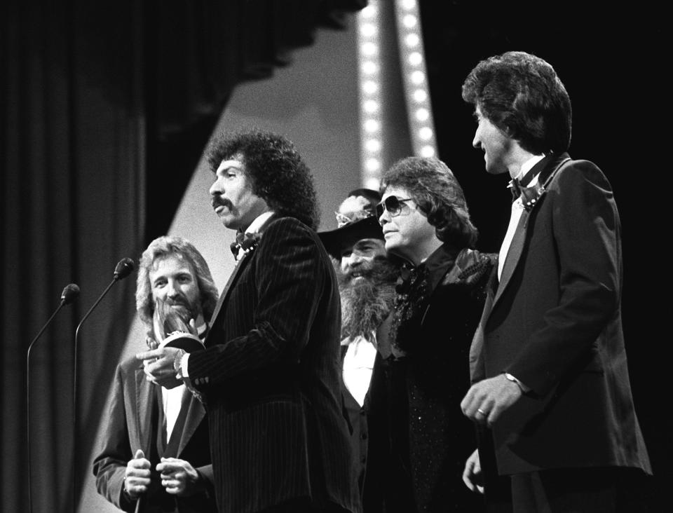 The Oak Ridge Boys members Duane Allen, left, Joe Bonsall, William Lee Golden and Richard Sterban, right, along with presenter Ronnie Milsap, second from right, are celebrating their Single of the Year award for "Elvira" during the 15th annual CMA Awards show nationally televised from the Grand Ole Opry House Oct. 12, 1981.