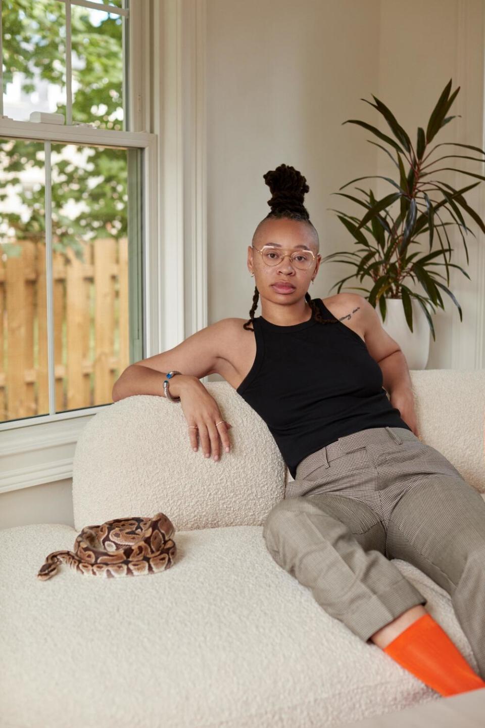 A woman sits on a beige couch next to a curled up snake