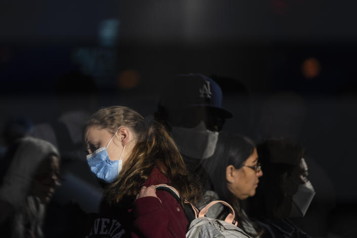 A woman wearing a blue face mask stands near another woman with no face mask.