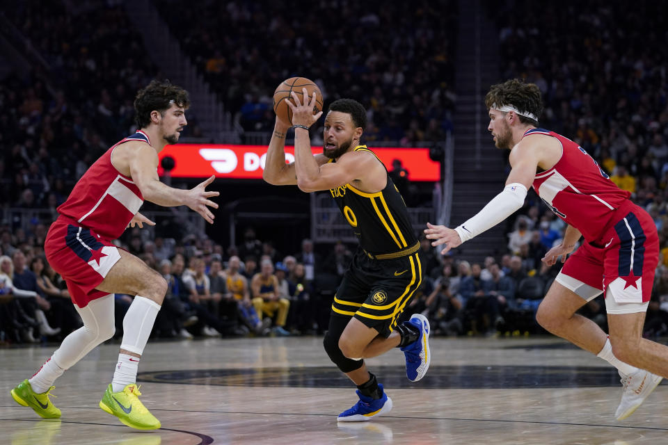 Golden State Warriors guard Stephen Curry, center, moves the ball between Washington Wizards forwards Deni Avdija, left, and Corey Kispert during the first half of an NBA basketball game Friday, Dec. 22, 2023, in San Francisco. (AP Photo/Godofredo A. Vásquez)