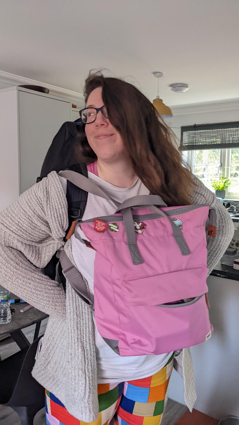 A woman smiling and carrying backpacks across the front and her back.