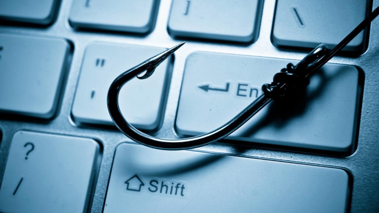  A fish hook is lying across a computer keyboard, representing a phishing attack on a computer system. 