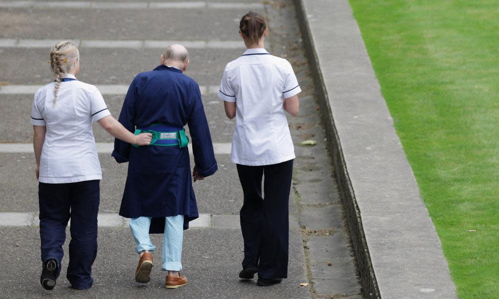 Two NHS staff walk with an elderly patient outside St Thomas’ Hospital in London