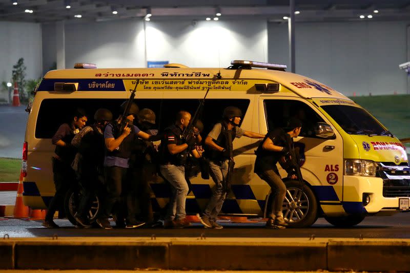 Thailand security forces take cover behind an ambulance as they chase a shooter hidden in a shopping mall after a mass shooting in front of the Terminal 21, in Nakhon Ratchasima, Thailand