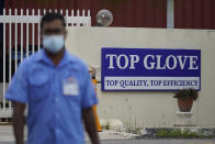 A worker from Top Glove walks outside Top Glove factory in Shah Alam, Malaysia, Wednesday, Nov. 25, 2020. Malaysia's Top Glove Corp., the world's largest maker of rubber gloves, says it expects a two to four-week delay in deliveries after more than 2,000 workers at its factories were infected by the coronavirus, raising the possibility of supply disruptions during the pandemic. (AP Photo/Vincent Thian)